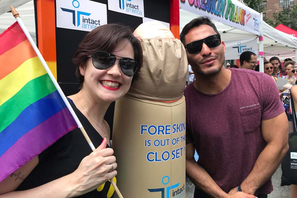 Couple standing with an inflatable penis with a sticker saying 'Foreskin is out of the closet'